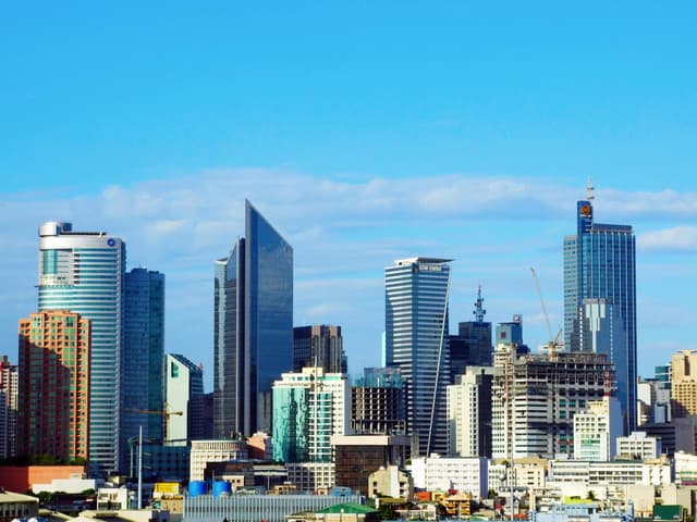 Bright daytime view of Makati City's modern skyline featuring prominent skyscrapers under a clear blue sky.