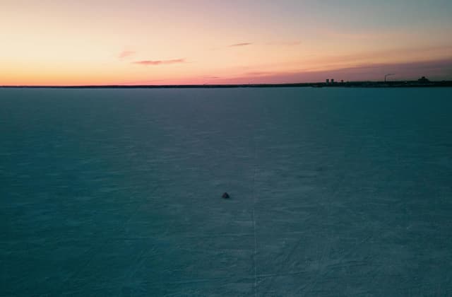 A tranquil winter sunset casts warm colors over a vast frozen lake in Novosibirsk, Russia.