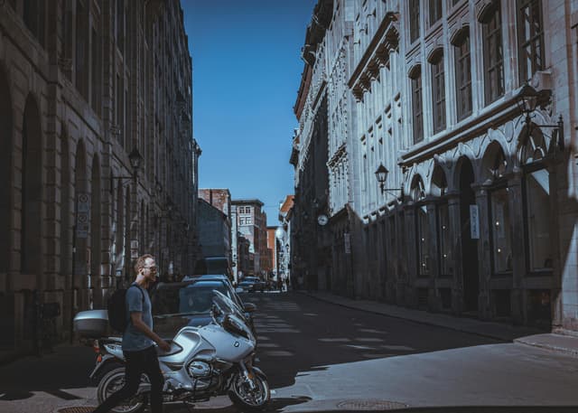 A man walking by a motorcycle on a shadowy street in Old Montreal with historic facades.