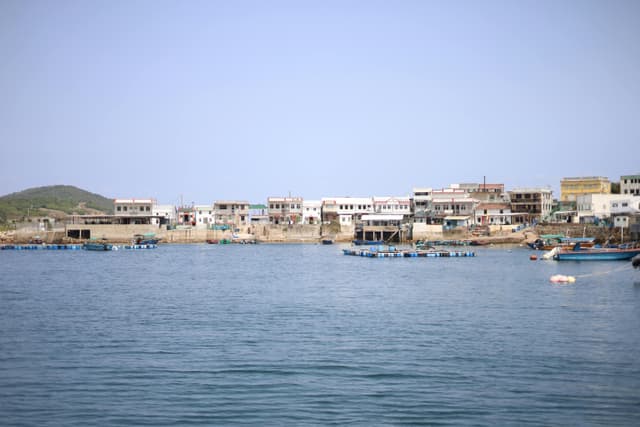 Scenic view of a fishing village along the Hong Kong coast with small boats and clear skies.