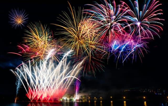 Spectacular fireworks light up the night sky over a calm Sherbrooke lake, celebrating a festive occasion.