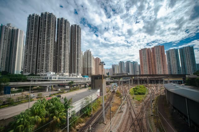 Dynamic cityscape of high-rise buildings and railways in Hong Kong under a partly cloudy sky.