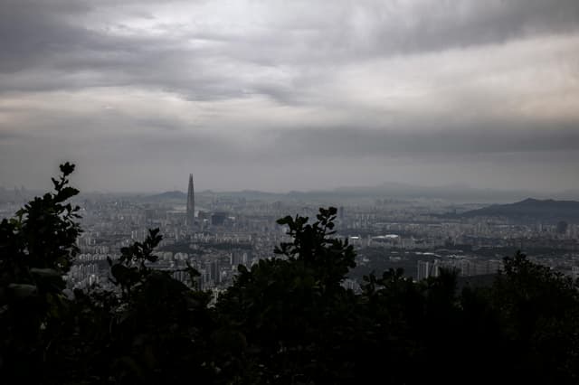 A dramatic aerial view of Gwangju cityscape with overcast skies and lush foreground.