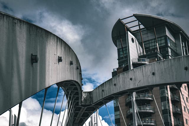 Dynamic shot of modern bridge and building facade under a cloudy sky in Salford, UK.