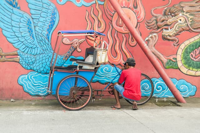 A vibrant bicycle rickshaw against dynamic street art in Makassar, Indonesia, capturing urban culture.