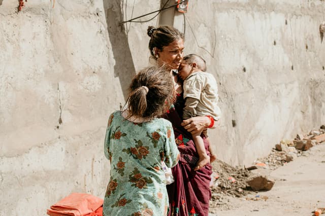 A mother holding her children on a sunlit street in Ujjain, India.