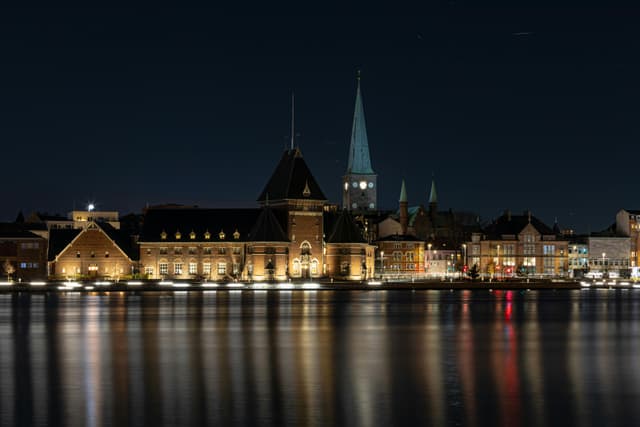 Scenic night view of Aarhus waterfront with illuminated historic buildings reflecting in the water.