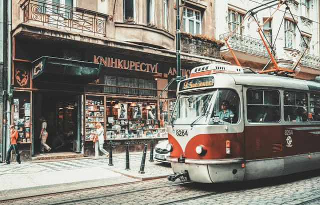 A vintage tram passes a historic bookstore on a vibrant street in Prague during summer.