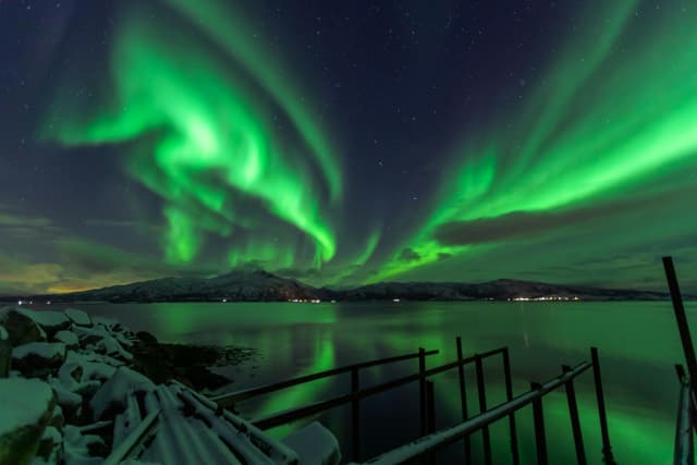 Dazzling Northern Lights illuminate a tranquil Lødingen fjord under a starry night.