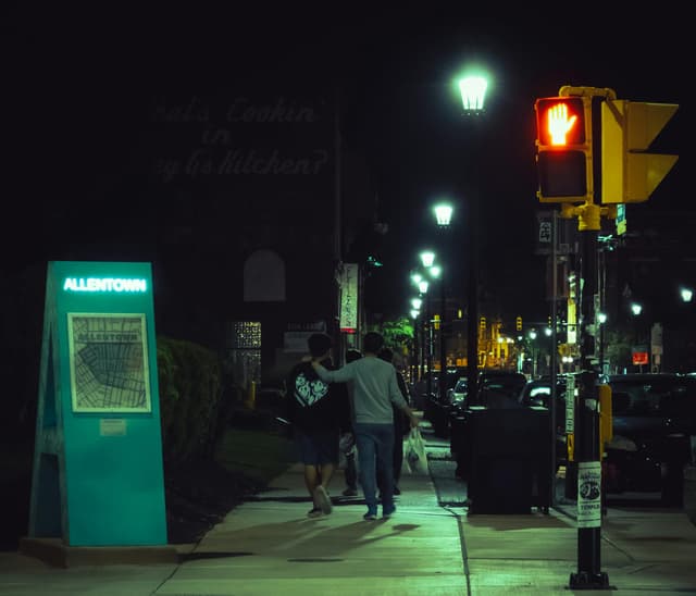 People walking on a lit sidewalk in Allentown at night, showcasing urban life.