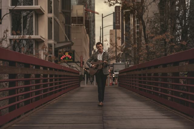 A man playing acoustic guitar on a city bridge at dusk, blending music with urban architecture.