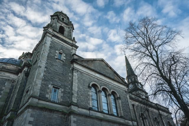 An imposing Gothic church in Edinburgh, Scotland featuring a striking clock tower against a bright sky.