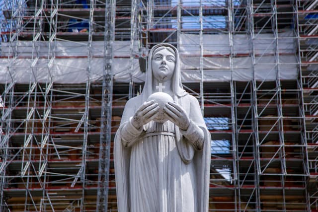 Statue of Virgin Mary holding an orb amidst scaffolding in Ho Chi Minh City, Vietnam.