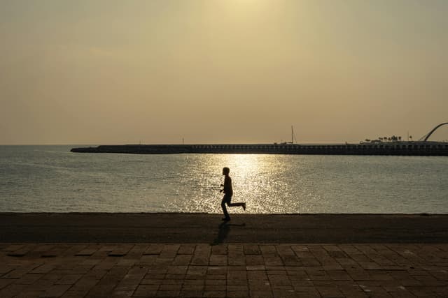 A man jogs along the Colombo promenade, silhouetted against the sunset over the ocean.
