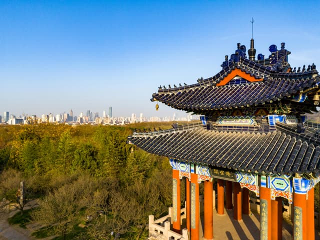 Scenic view of a traditional Chinese pavilion with the Nanjing city skyline in the background.