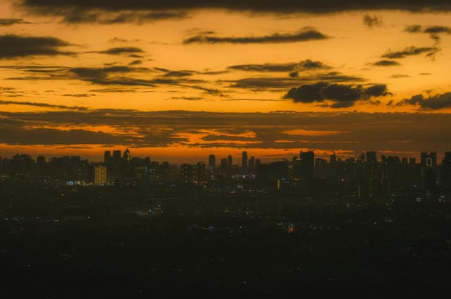 Capture of Antipolo city skyline silhouetted against a warm, orange sunset.