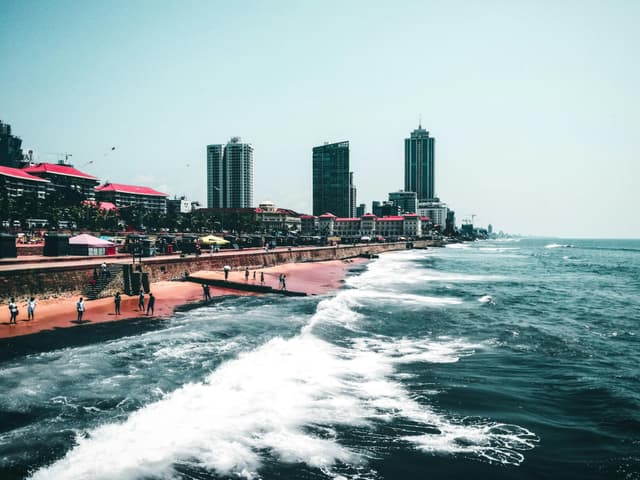 Scenic view of a coastal city with tall buildings and waves crashing against the shore.