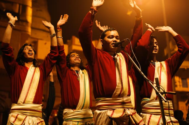Group of men in traditional attire singing with raised hands in Varanasi, India.
