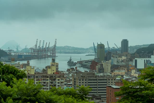 Scenic aerial view of Keelung Harbor, Taiwan with modern architecture and cranes under overcast skies.