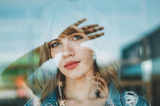 Creative portrait of a woman with reflections in glass, featuring star earrings.