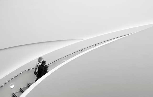 Two people on a sleek staircase, minimalistic architecture in black and white.