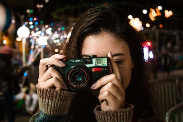 A woman captures moments with a vintage camera in an urban night setting.