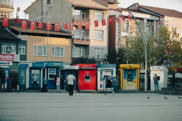 Street view in Bartın, Türkiye with ATMs, people, and waving Turkish flags.