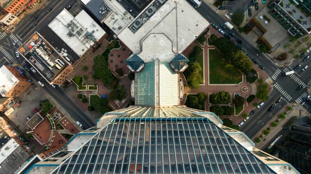 High angle shot of a modern skyscraper surrounded by urban streets and lush greenery from above.