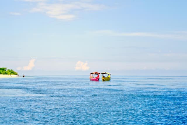 Two traditional boats on clear turquoise waters near a tropical beach in Zamboanga, Philippines.