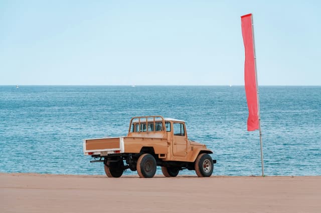Retro truck parked on the beach of Khor Fakkan with a red flag, overlooking the ocean.