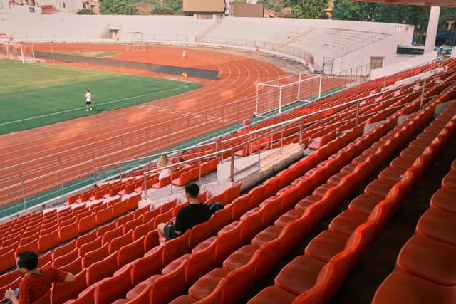 People watching a football practice at Hải Phòng stadium in Vietnam. Sunlit empty seats create a captivating scene.