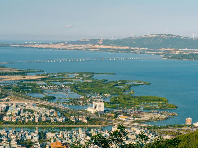 Scenic aerial view of Quy Nhơn, featuring ocean, islands, wind turbines, and vibrant cityscape.