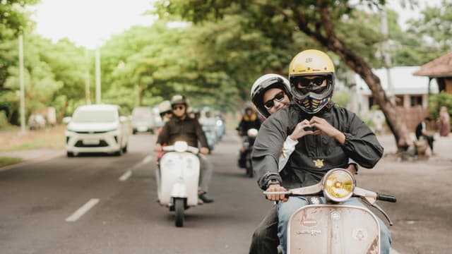 A joyful couple riding a Vespa on a tree-lined street in East Java, Indonesia.