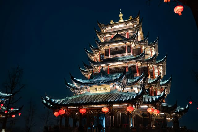 Illuminated traditional Chinese temple in Chongqing, adorned with red lanterns during night time.