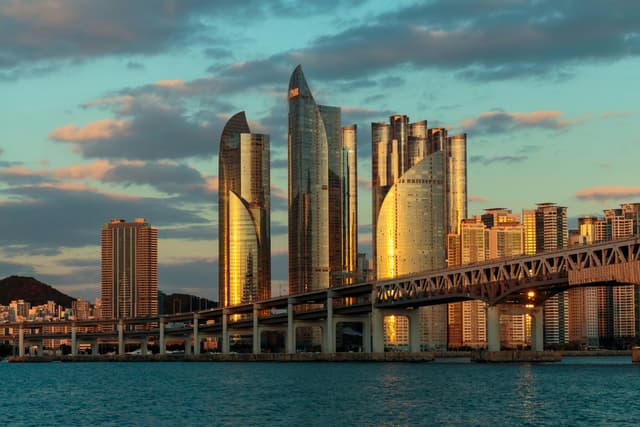 A stunning sunset view of the Busan skyline with bridge and skyscrapers reflecting sunlight.