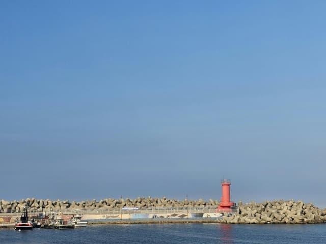 A vivid red lighthouse surrounded by tetrapods at Ulsan Harbor under a clear blue sky.