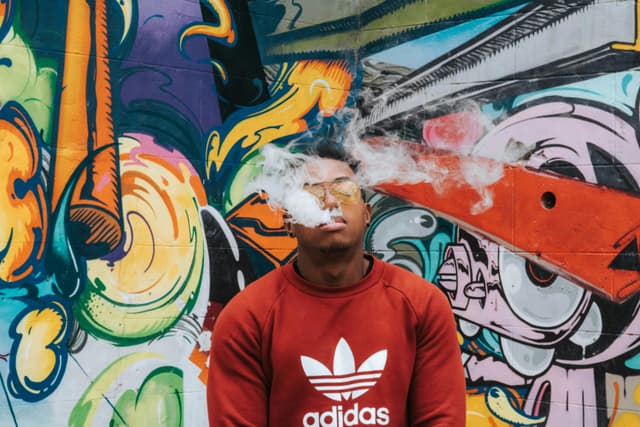 Man in casual wear smoking in front of colorful graffiti wall in Richmond, VA.