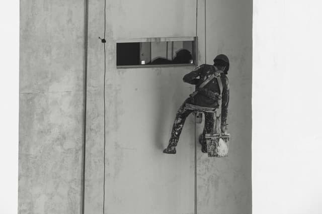 A painter suspended on a building facade in Aracaju, Brazil, performing high-risk maintenance.