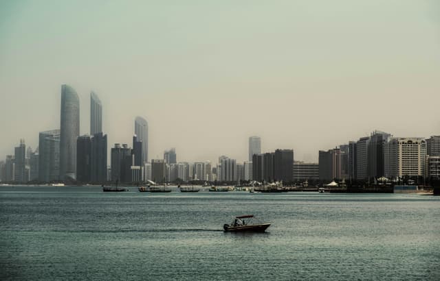 Distant view of Abu Dhabi skyline across the water with boats. Calm and serene urban landscape.
