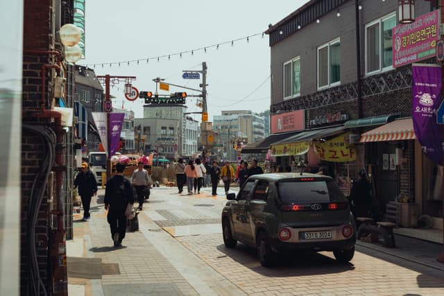Explore a bustling street scene in Suwon, South Korea, featuring people, shops, and vibrant signage.