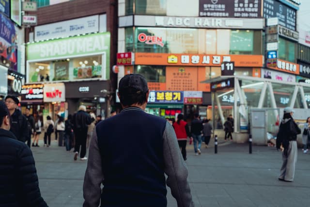 A vibrant street view of Suwon, South Korea with people and colorful shop signs.