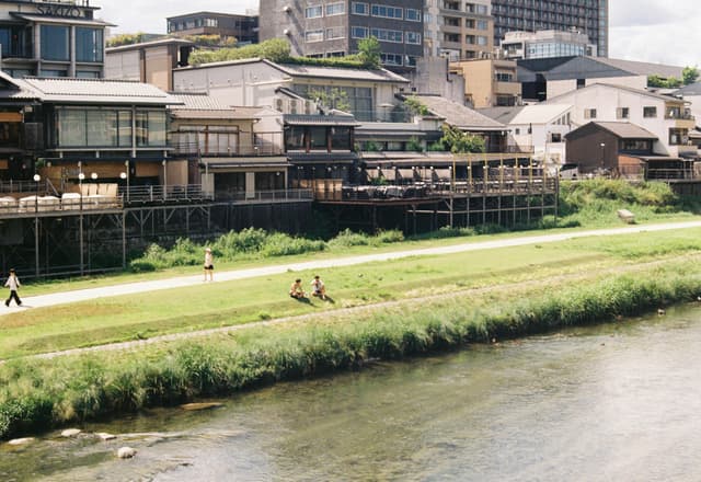 Serene view of Kyoto riverbank with traditional buildings and lush greenery.