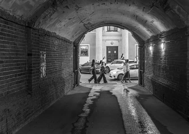 Monochromatic view through a tunnel with people walking outside.