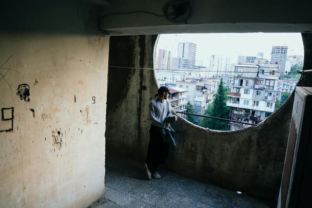 A person stands on a rustic balcony overlooking T'bilisi, Georgia's cityscape.