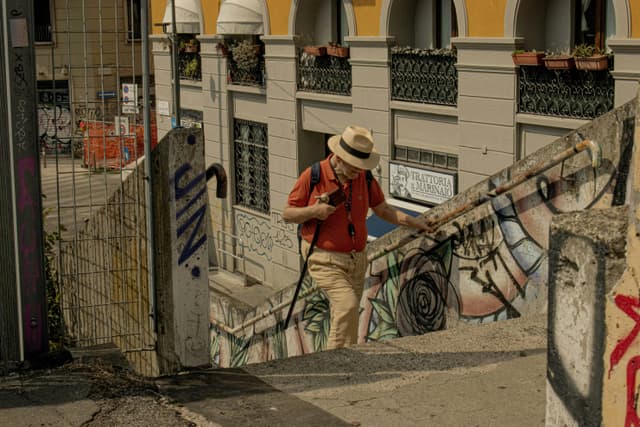 A man in a hat climbs an outdoor staircase covered in graffiti, urban setting.