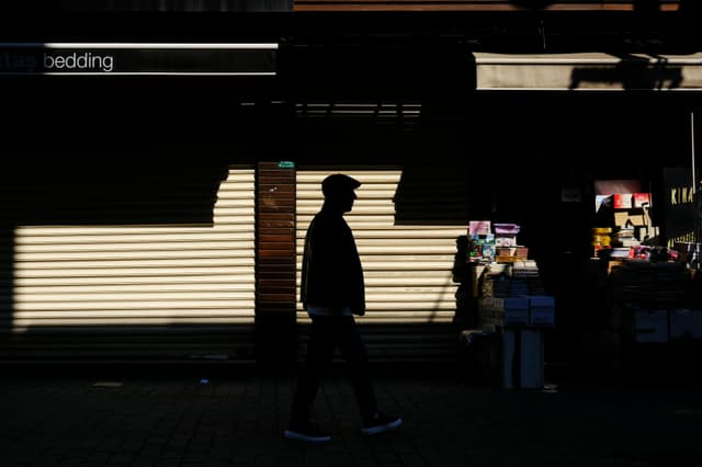 A silhouetted man walks past closed shops in Bursa, Türkiye, captured in dramatic shadows.