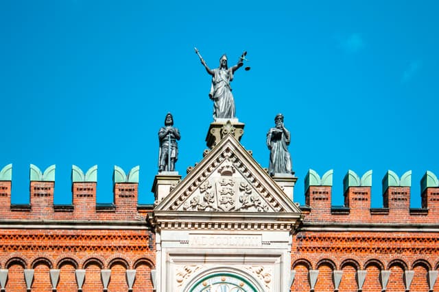 Stunning facade of Odense courthouse with Lady Justice statue under clear blue skies.