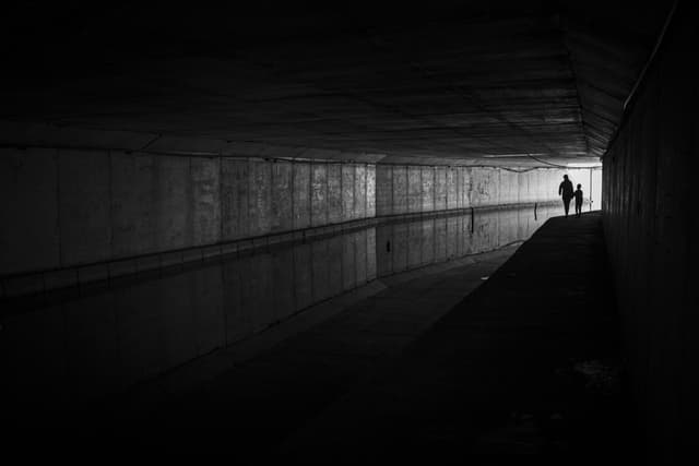 Moody black and white photo of silhouettes walking in tunnel.