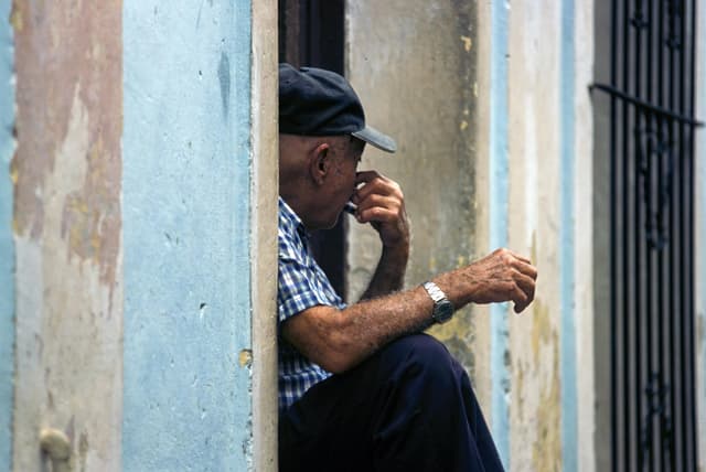 Portrait of an elderly man sitting in a doorway in Cuba, capturing a moment of reflection.