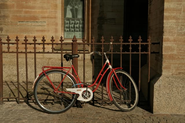 A classic red bicycle leaning against an ornate fence on a sunny day in Linköping, Sweden.